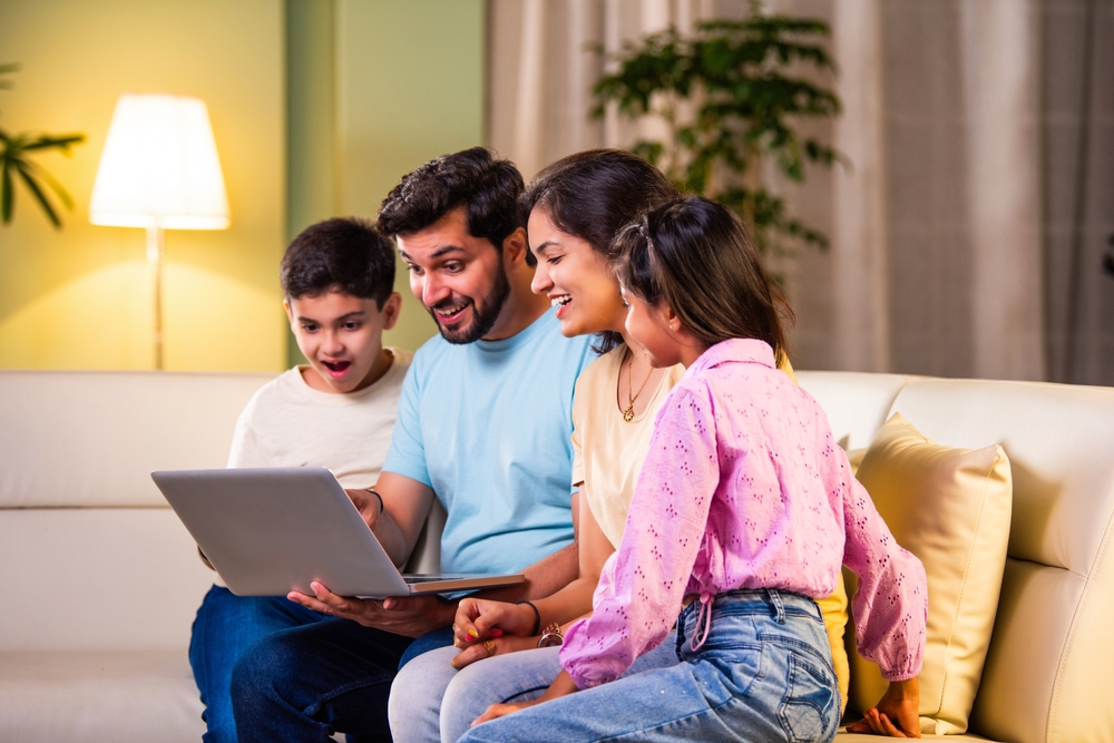 Indian,Asian,Young,Family,Of,Four,Sitting,On,A,Sofa,