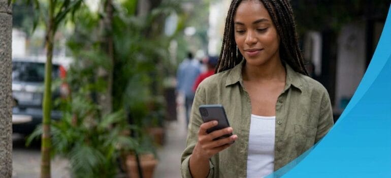 Woman on a city sidewalk checking a payment text on her smartphone
