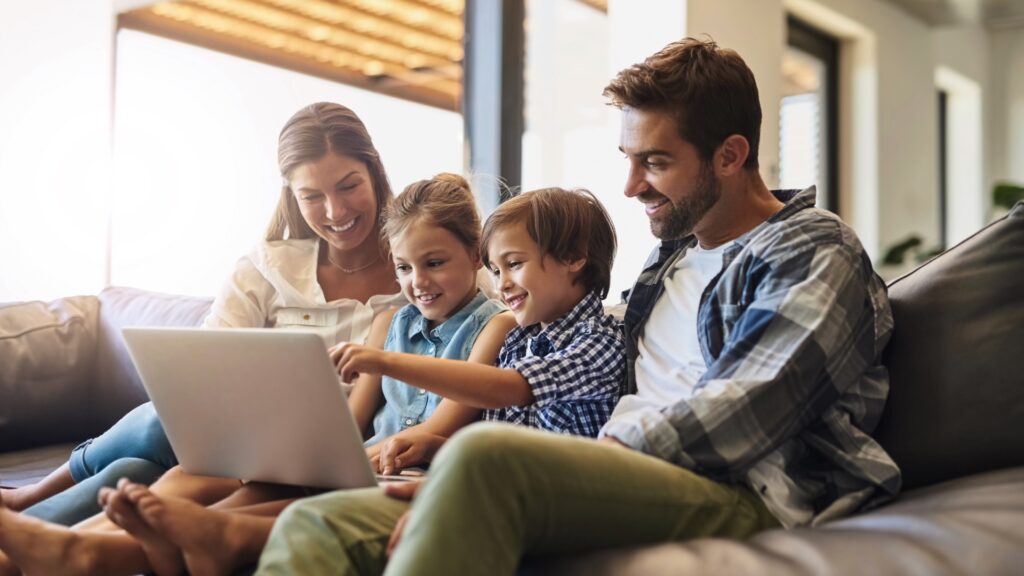 A family smiling together at a laptop on the couch